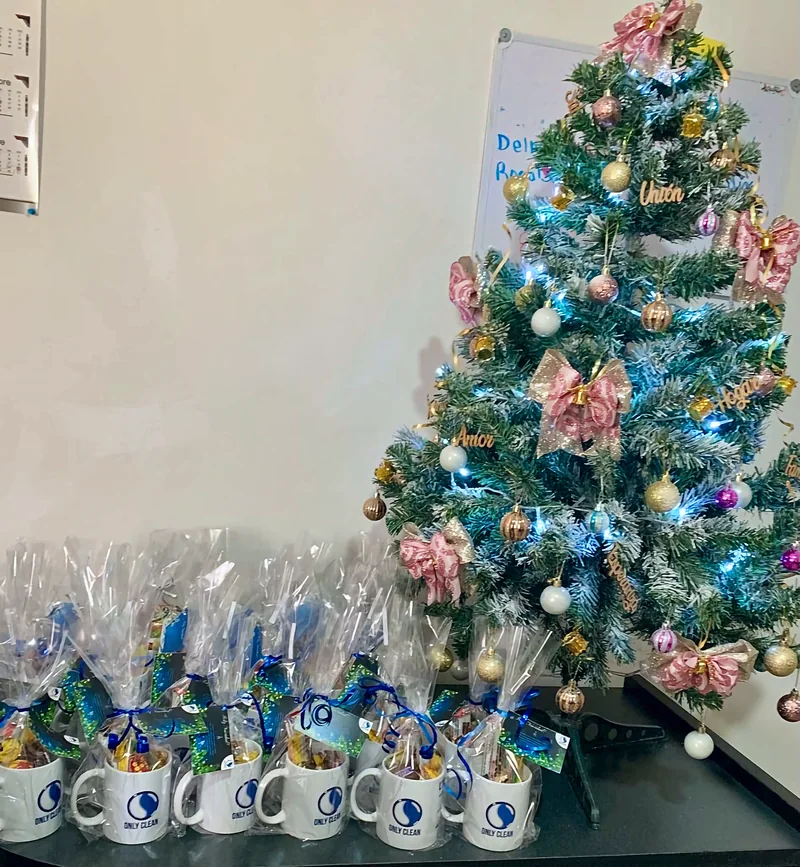 Tazas de regalo de Only Clean con dulces junto al árbol de Navidad, para el personal de limpieza